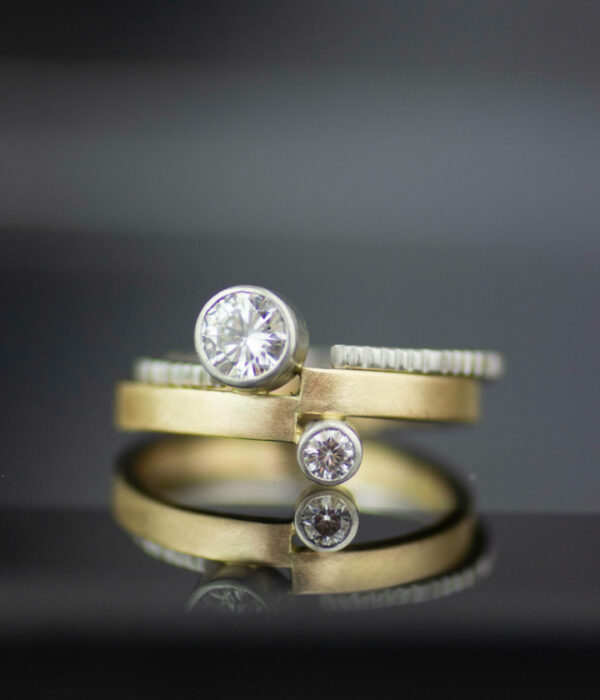 mixed metals bezel set moissanite in platinum and 14K yellow gold asymmetrical engagement ring with textured wedding band