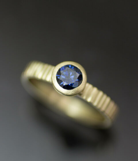 a deep blue moissanite gemstone and yellow gold band in a simple wedding & engagement ring design.