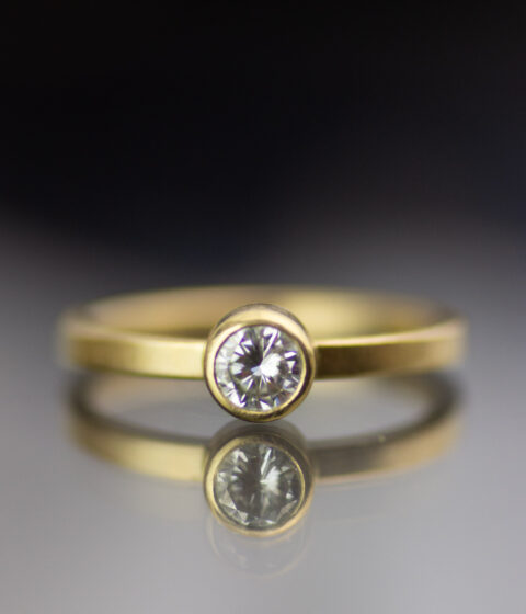 yellow gold band with a white moissanite gemstone in a simple, modern design.