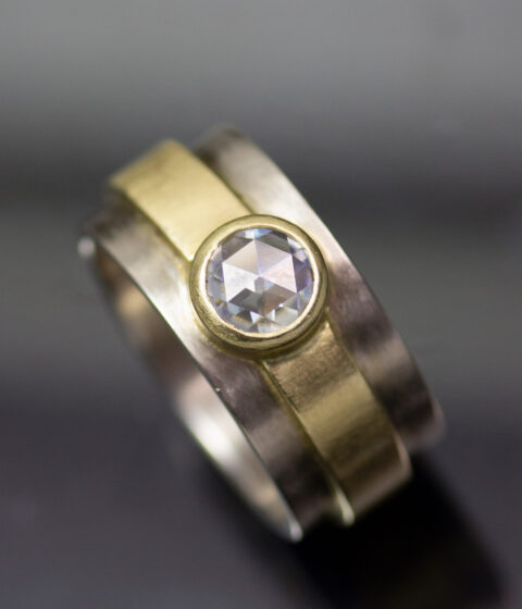 A thick banded wedding ring made with layers of white gold, yellow gold, and a centered rose-cut moissanite gemstone.