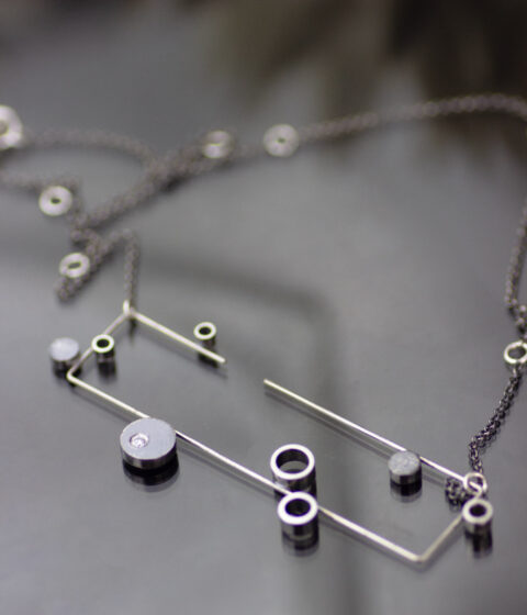 A rectangular necklace pendant made of oxidized sterling silver and platinum in a geometric design